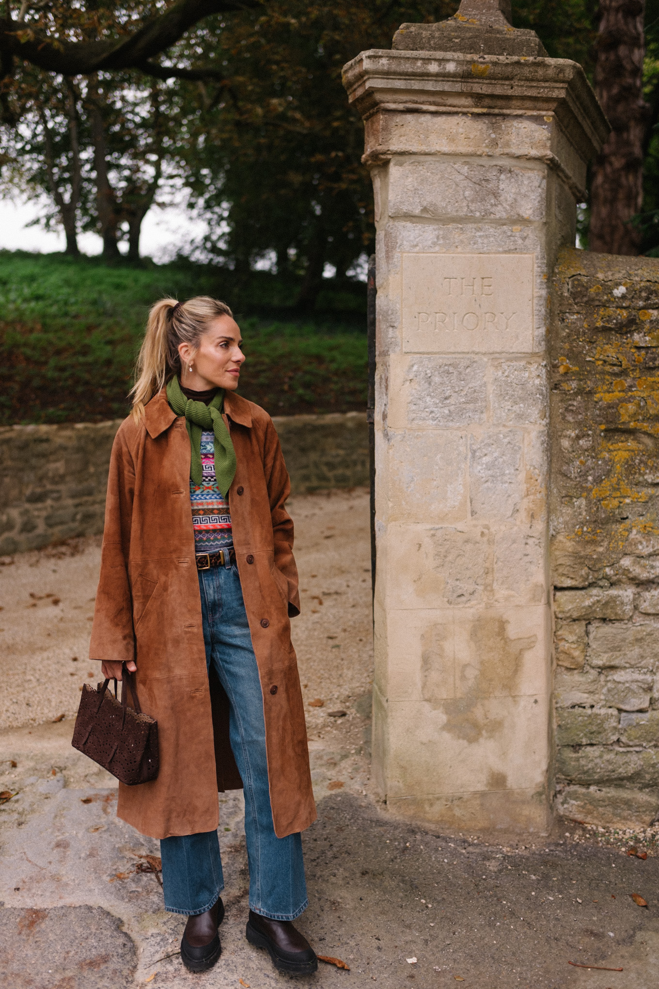 Manteau d'hiver en daim marron, pull en jacquard, gilet, écharpe verte, jean bleu, bottes marron