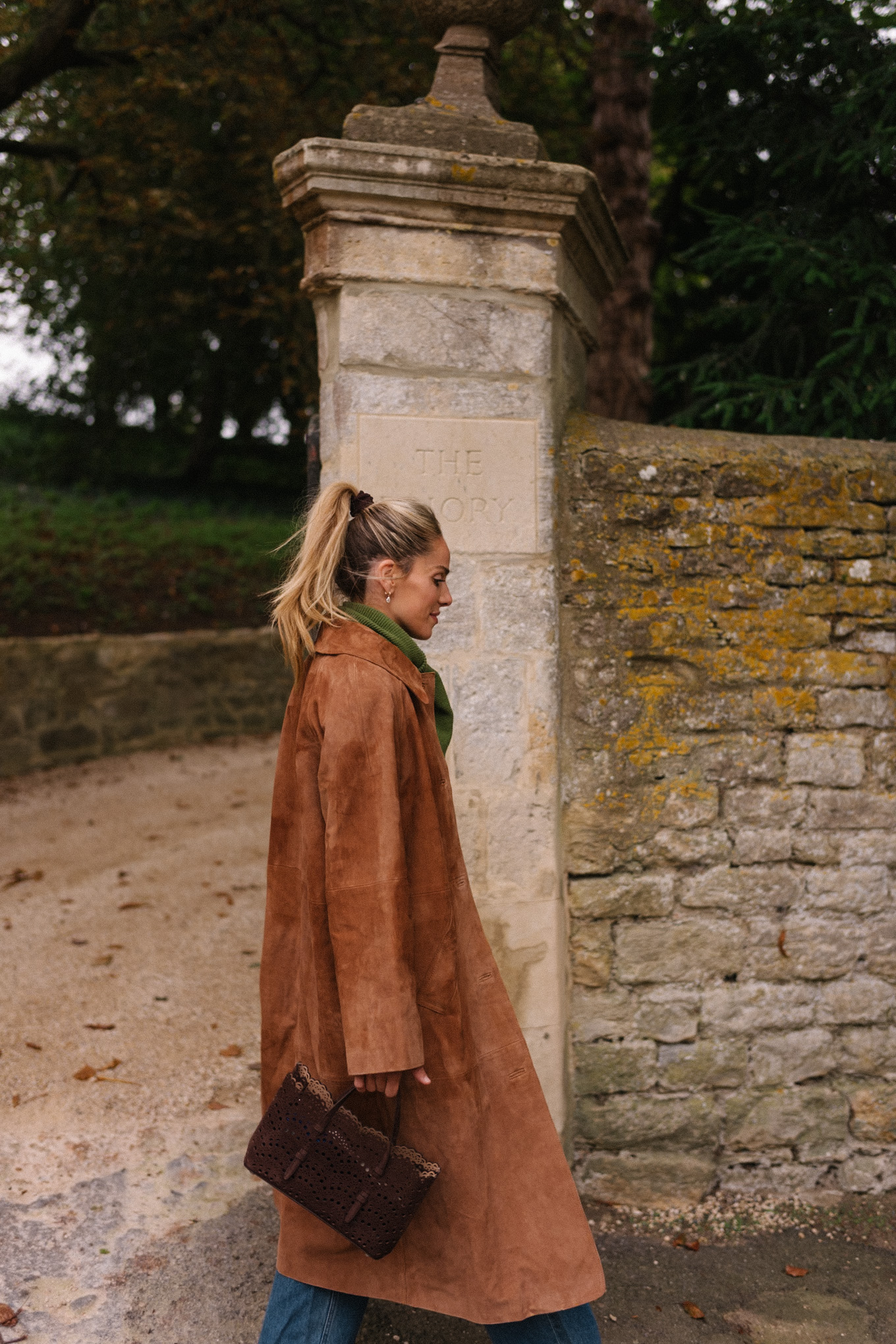 Manteau d'hiver en daim marron, pull en jacquard, gilet, écharpe verte, jean bleu, bottes marron