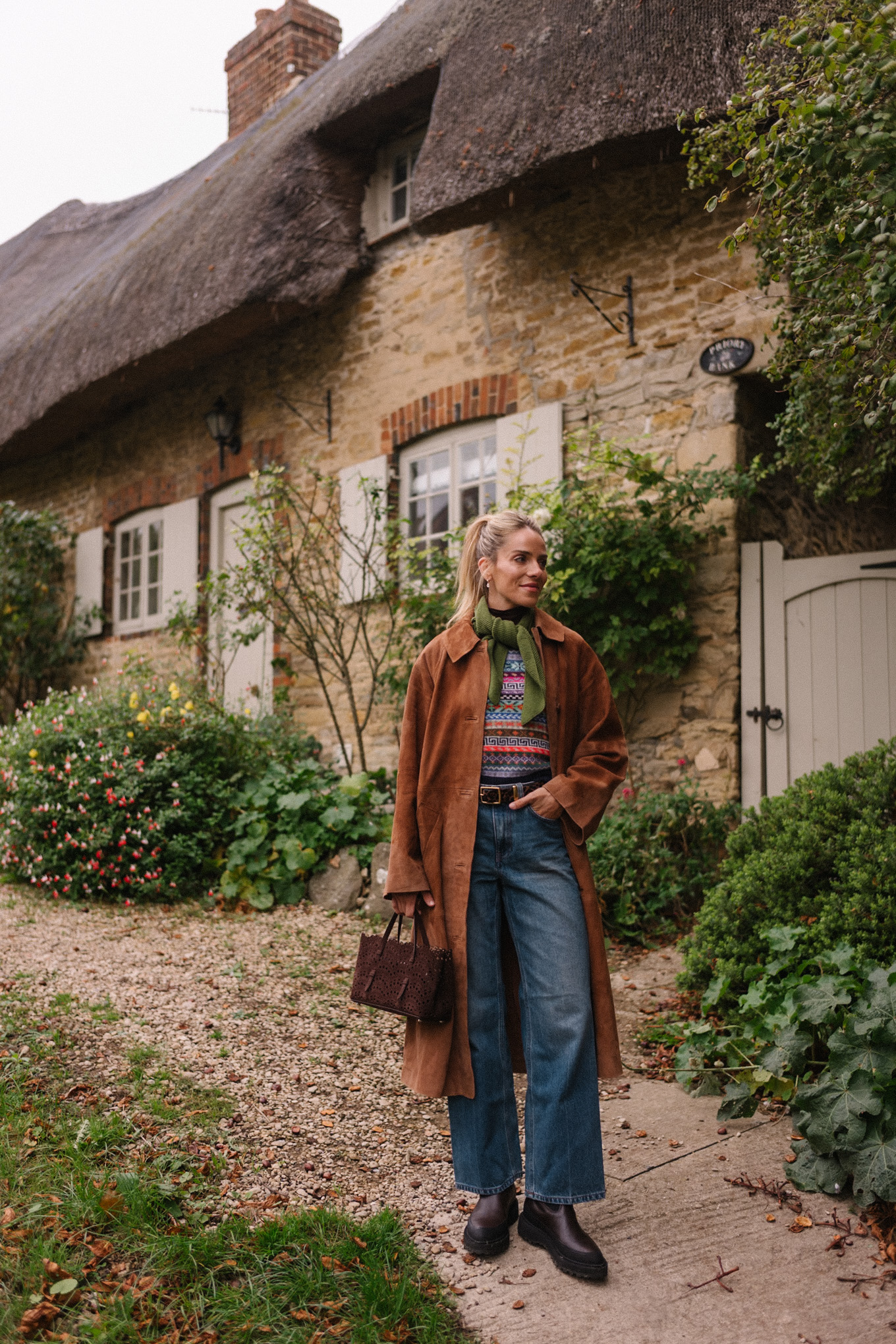 Manteau d'hiver en daim marron, pull en jacquard, gilet, écharpe verte, jean bleu, bottes marron