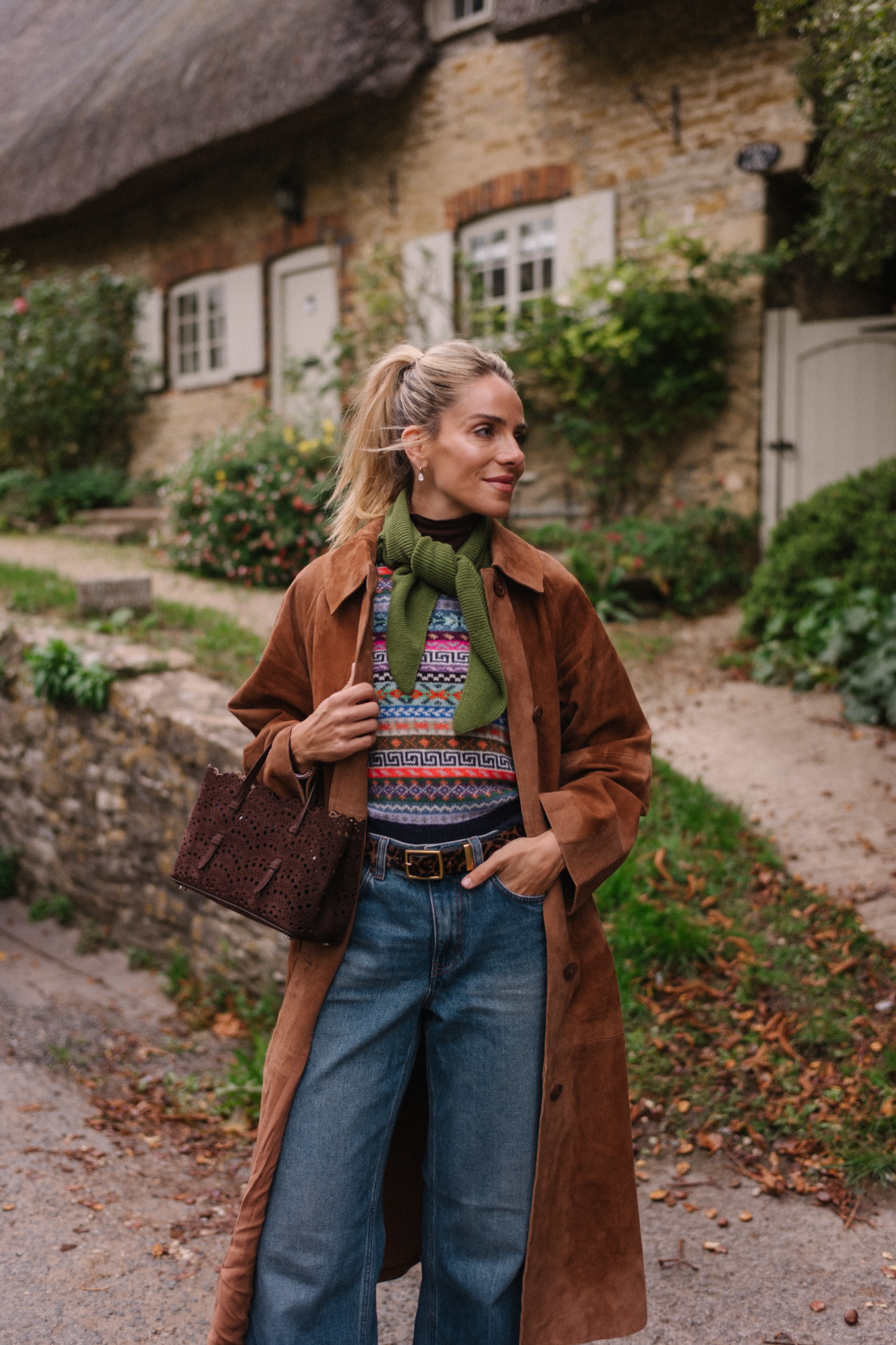 Manteau d'hiver en daim marron, pull en jacquard, gilet, écharpe verte, jean bleu, bottes marron