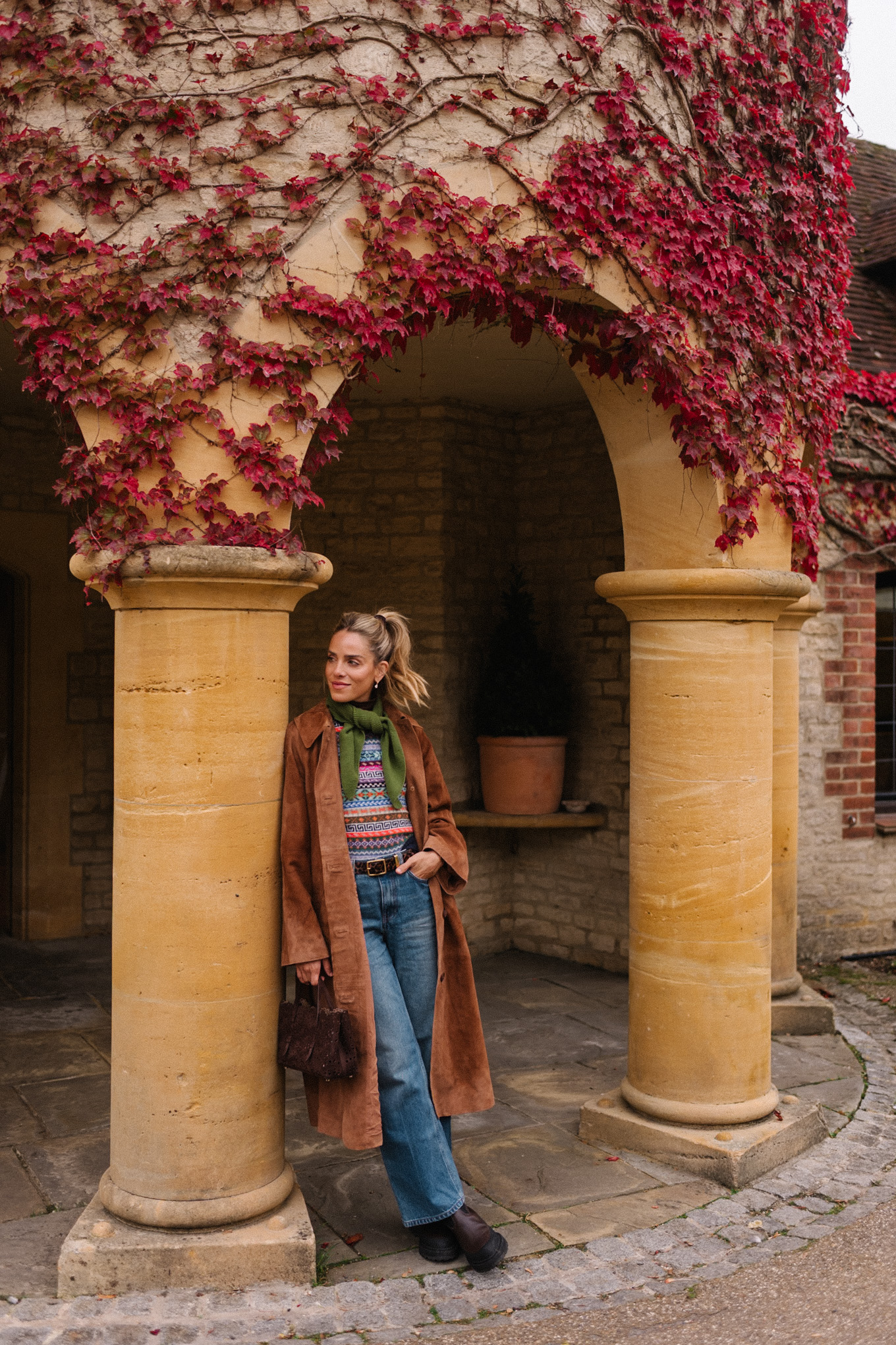 Manteau d'hiver en daim marron, pull en jacquard, gilet, écharpe verte, jean bleu, bottes marron