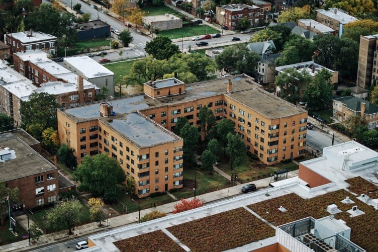 A large, U-shaped apartment building made of tan brick in an urban setting as seen from above.