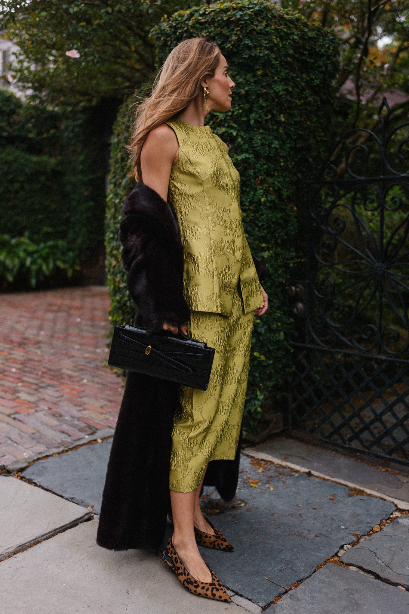 L'ensemble comprend un haut et une jupe chartreuse, un long manteau noir, un sac à main noir et des escarpins léopard