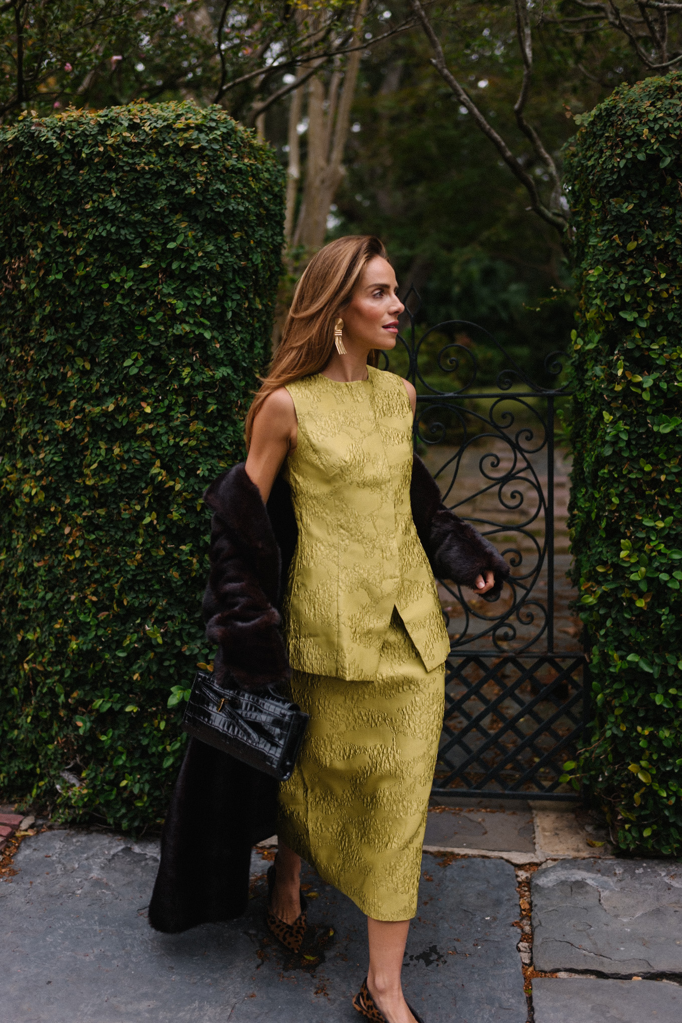 L'ensemble comprend un haut et une jupe chartreuse, un long manteau noir, un sac à main noir et des escarpins léopard