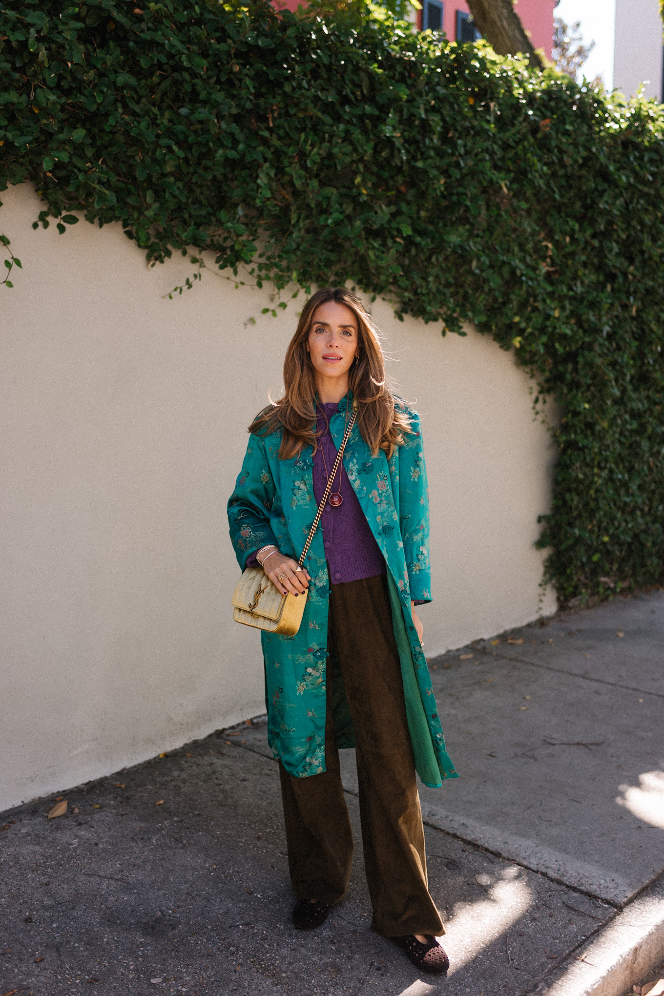 manteau en soie bleu sarcelle, pull en cachemire violet, pantalon en daim marron, sac en daim doré, ballerines marron