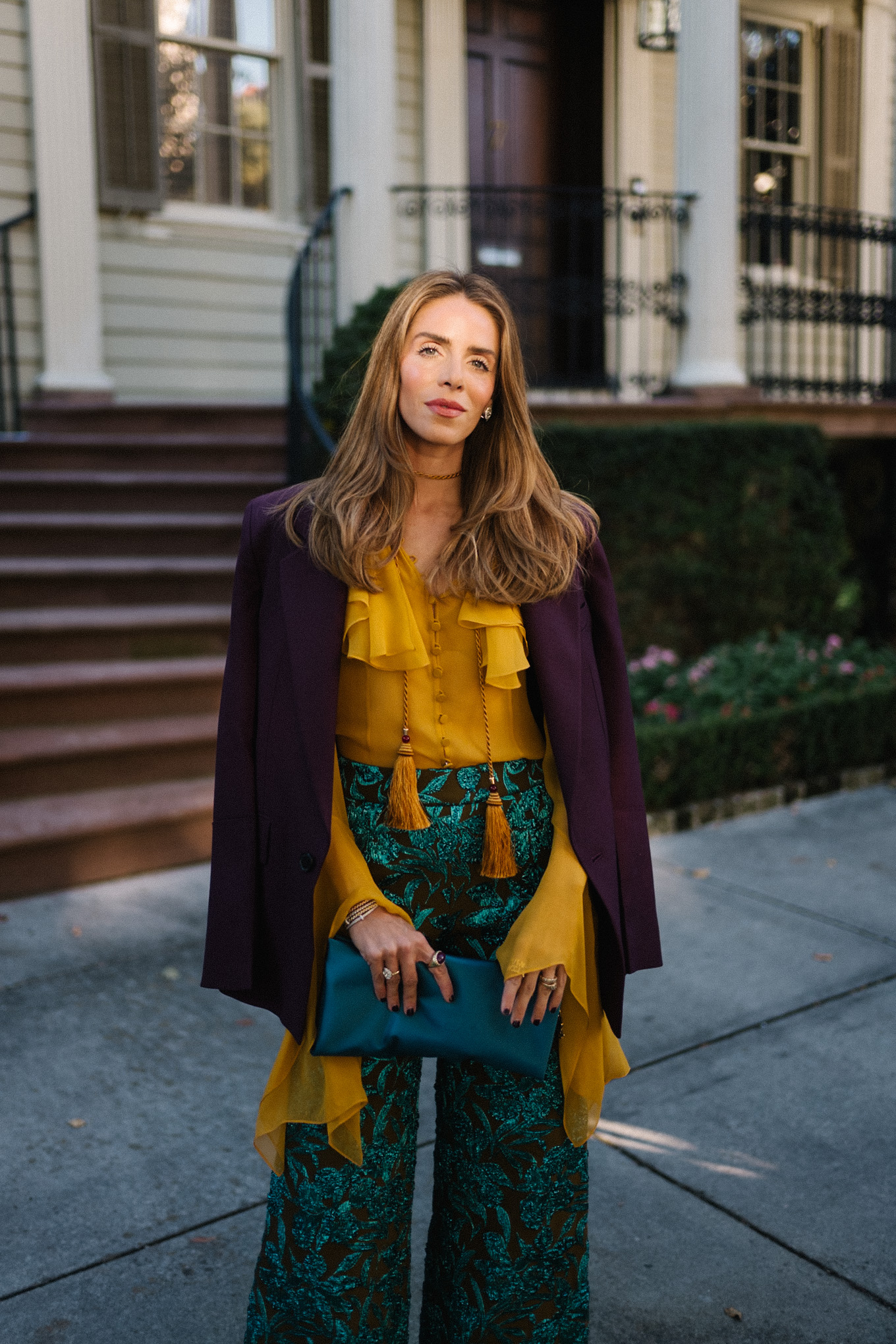 Blazer prune, chemisier à volants dorés, pantalon jacquard, pochette turquoise, escarpins violets