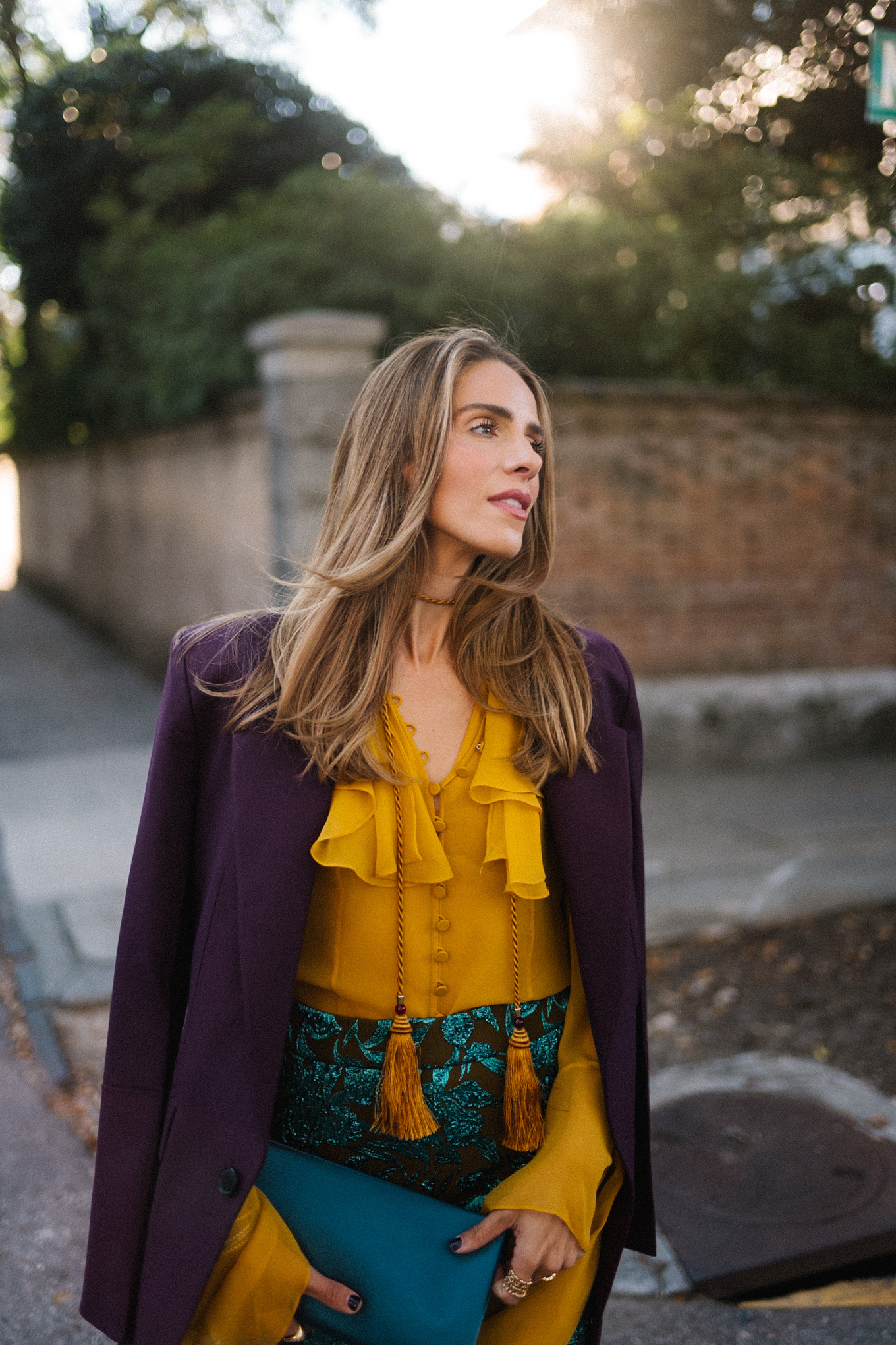 Blazer prune, chemisier à volants dorés, pantalon jacquard, pochette turquoise, escarpins violets