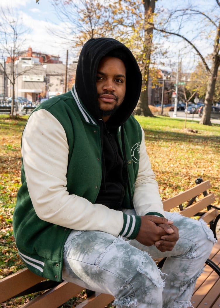 A man wearing jeans and a hooded sweatshirt sits on top of a park bench.