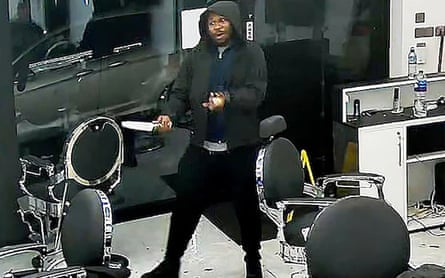 Un homme en sweat à capuche noir tient un grand couteau dans le salon de coiffure