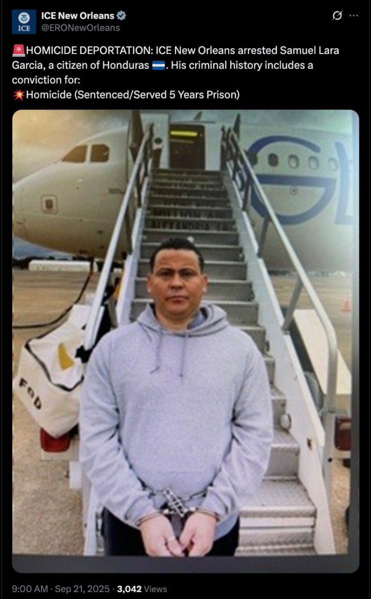 Ein grau gekleideter Mann blickt in die Kamera. Seine Hände sind gefesselt. Hinter ihm führt eine Treppe hinauf zu einem Flugzeug.