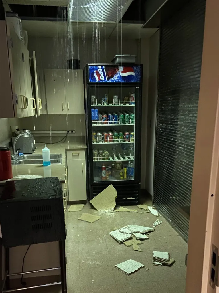 Water leaks from a ceiling and floods a room with ceiling tiles on the floor.