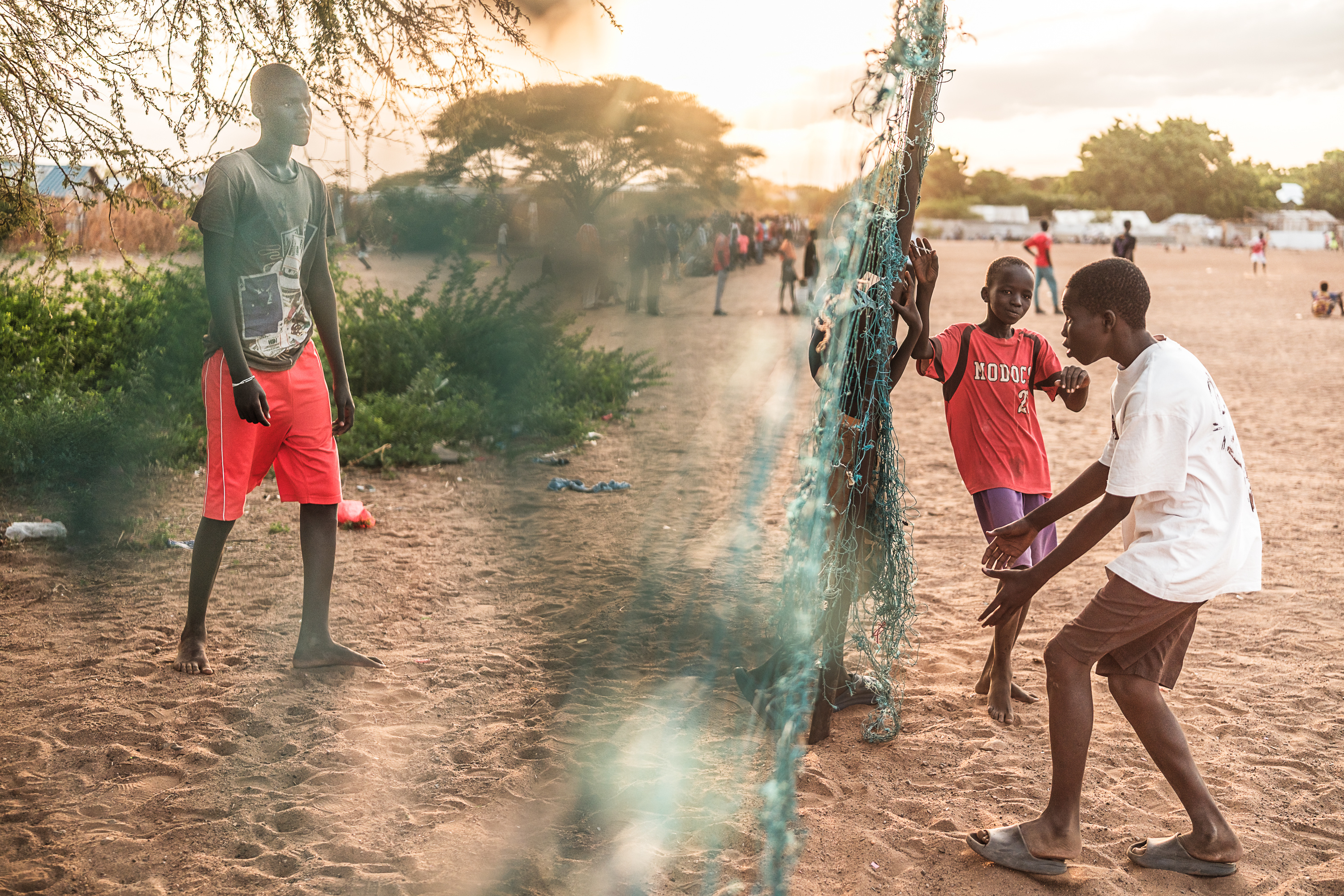 Several boys hang out around a tattered net while other boys play soccer in the background.