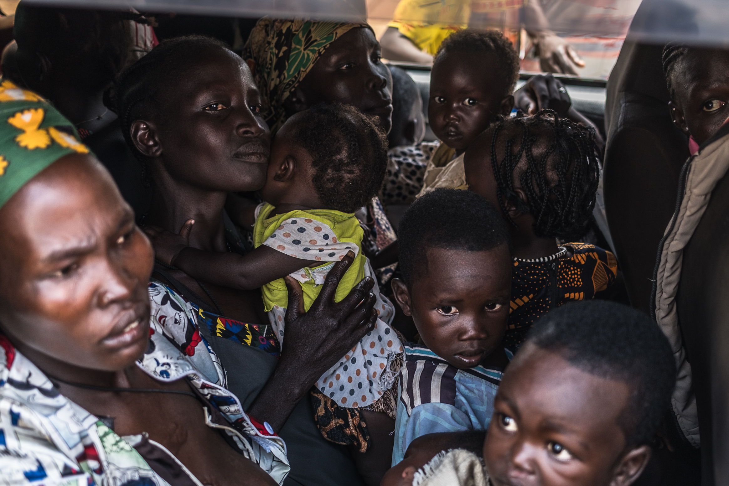 Women and children are packed tightly into the back of a car.