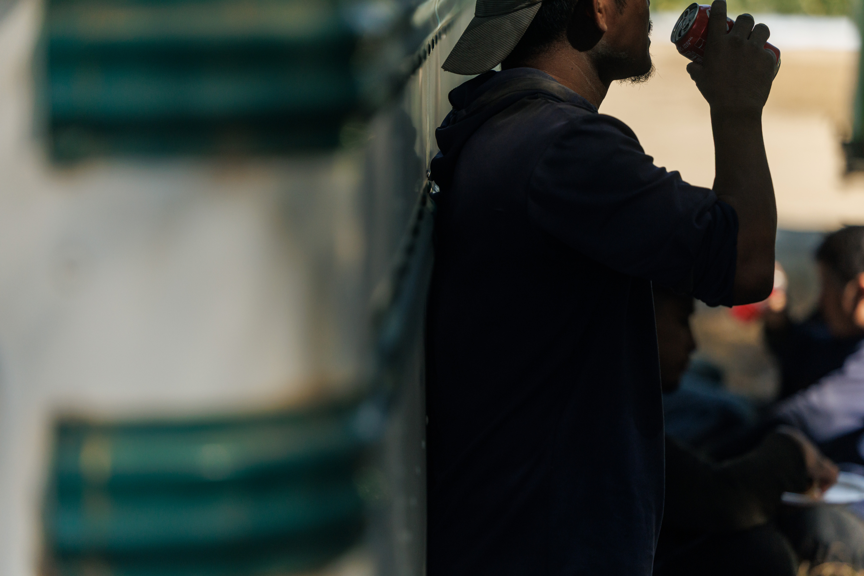 A man drinks a canned beverage while leaning against a bus.