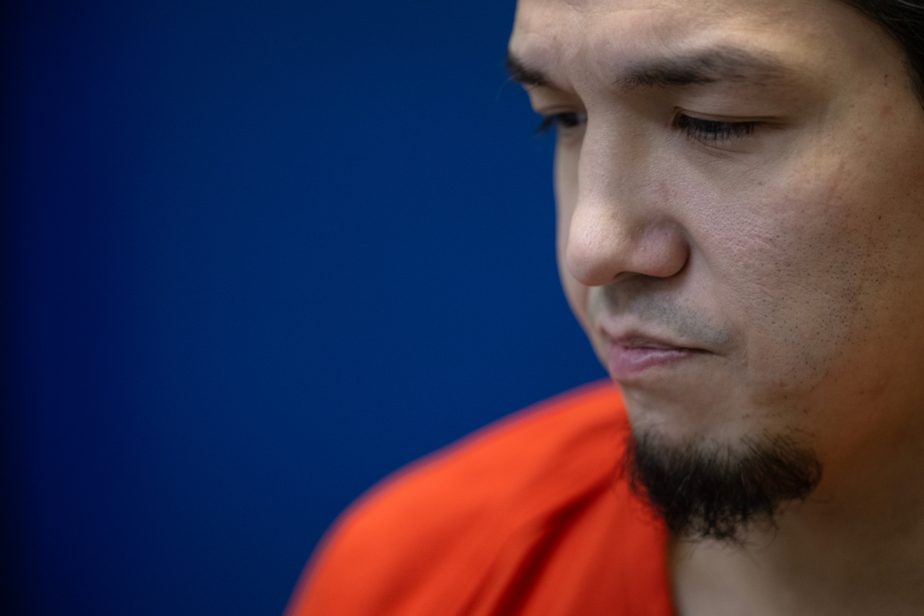 A man with a goatee wearing an orange shirt stares off camera.