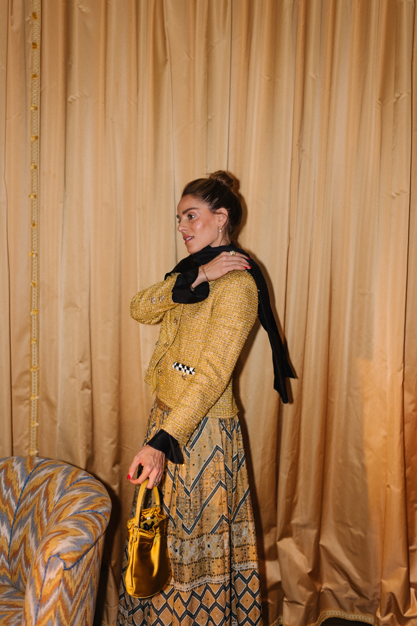 Veste en tweed doré, jupe imprimée dorée, sac seau en soie dorée, écharpe noire, bottes noires