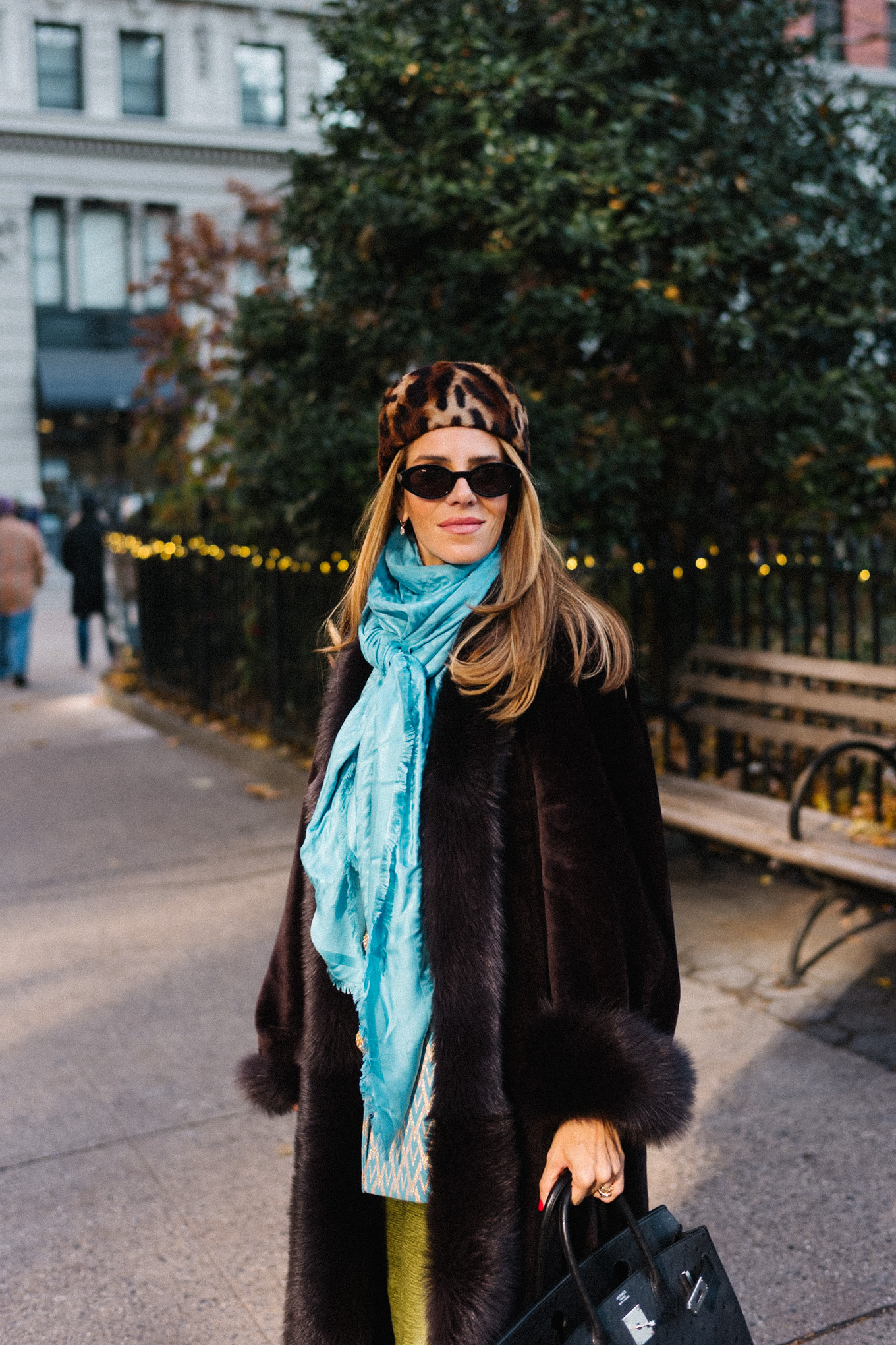 Manteau en peau lainée marron, chapeau casemate imprimé léopard, pantalon en satin vert, foulard en soie turquoise
