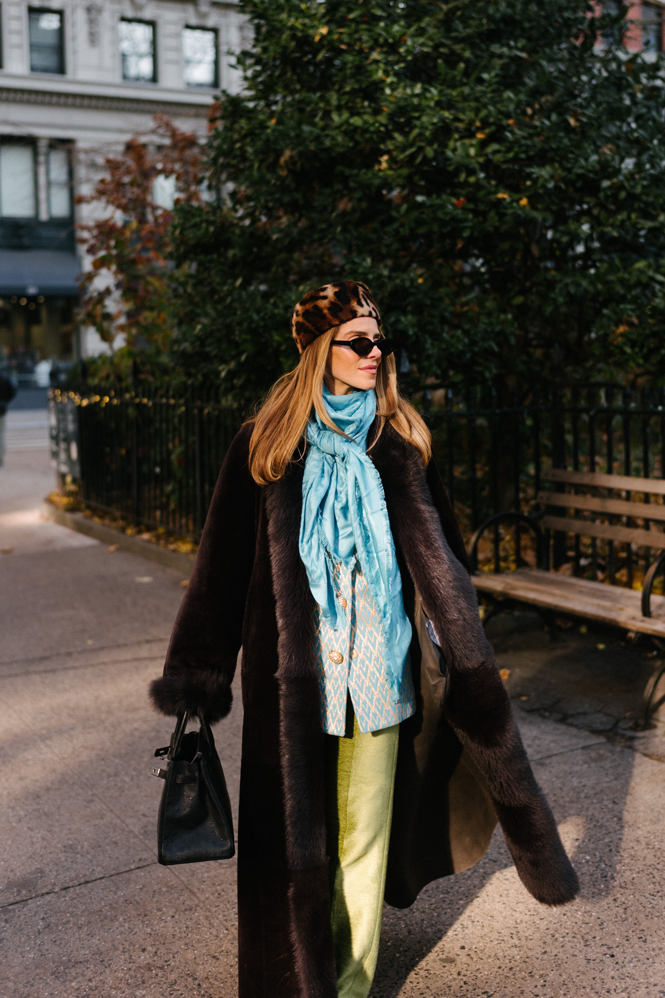 Manteau en peau lainée marron, chapeau casemate imprimé léopard, pantalon en satin vert, foulard en soie turquoise