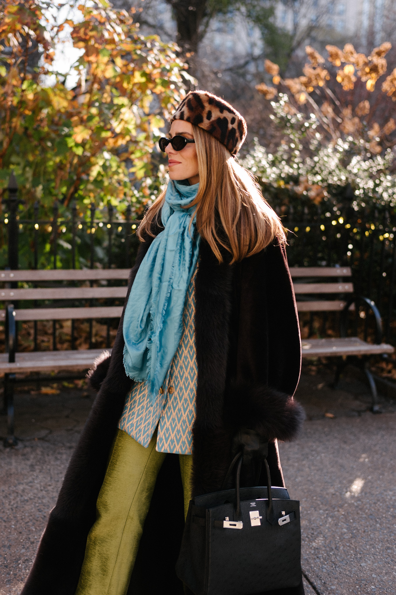 Manteau en peau lainée marron, chapeau casemate imprimé léopard, pantalon en satin vert, foulard en soie turquoise