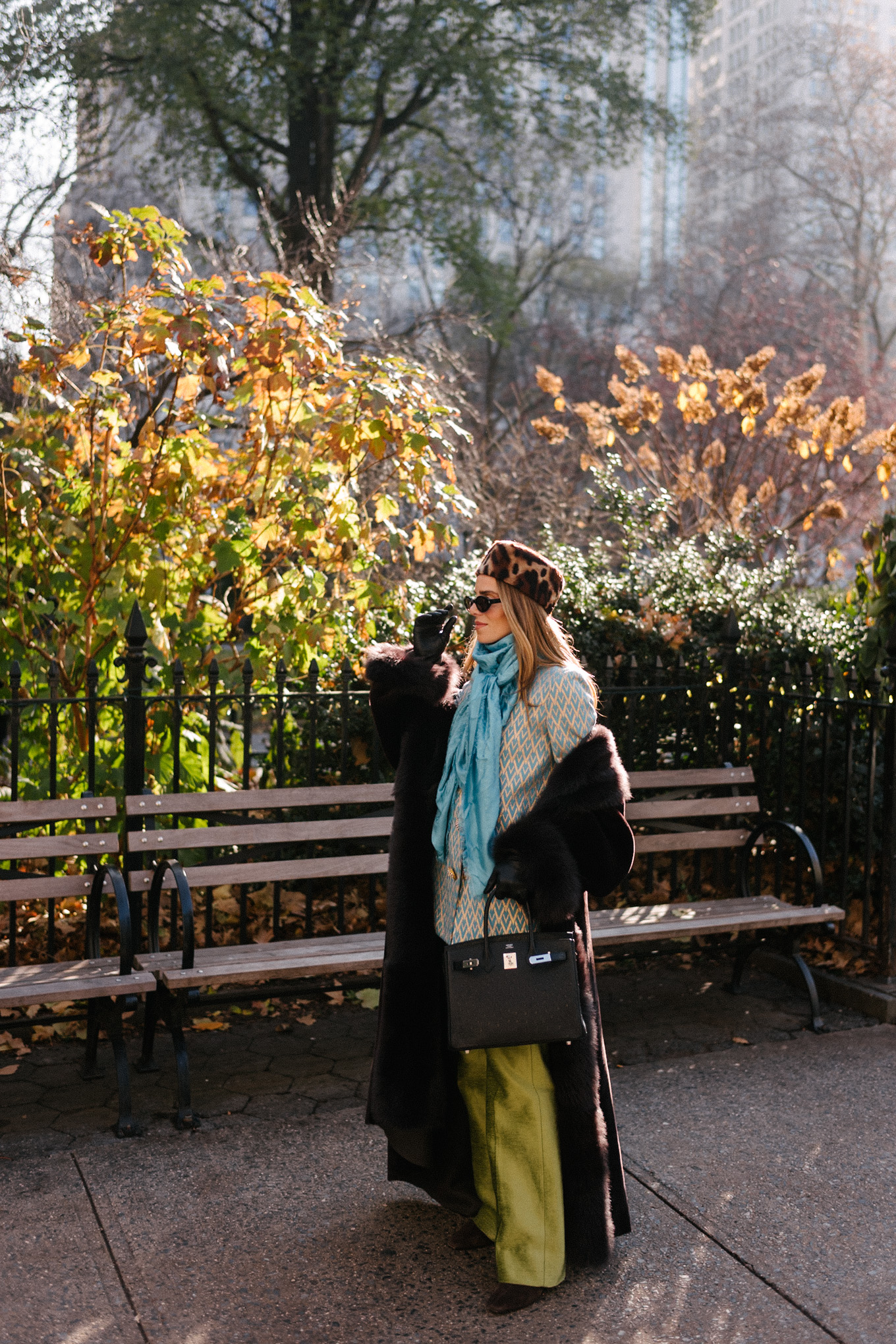 Manteau en peau lainée marron, chapeau casemate imprimé léopard, pantalon en satin vert, foulard en soie turquoise
