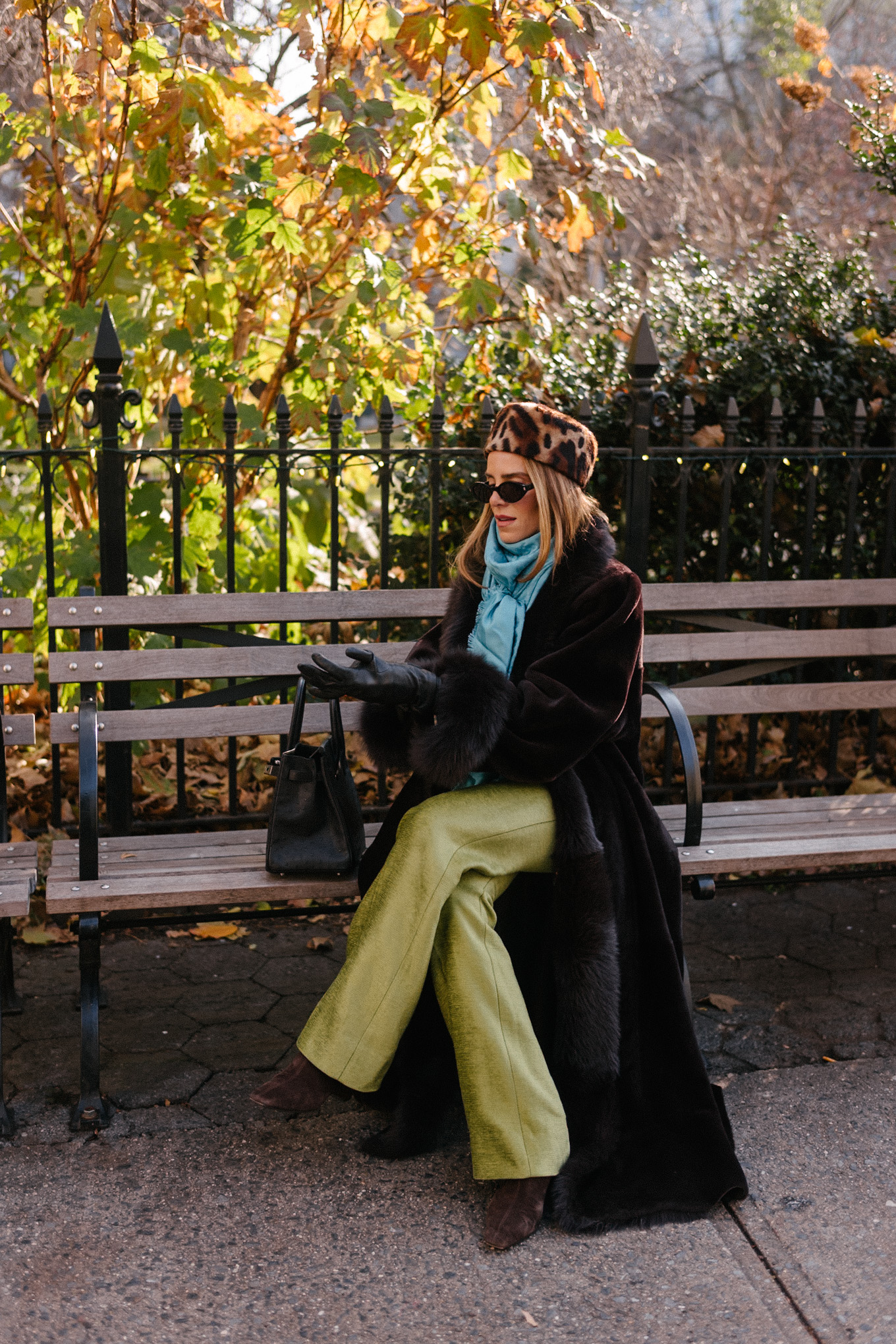 Manteau en peau lainée marron, chapeau casemate imprimé léopard, pantalon en satin vert, foulard en soie turquoise