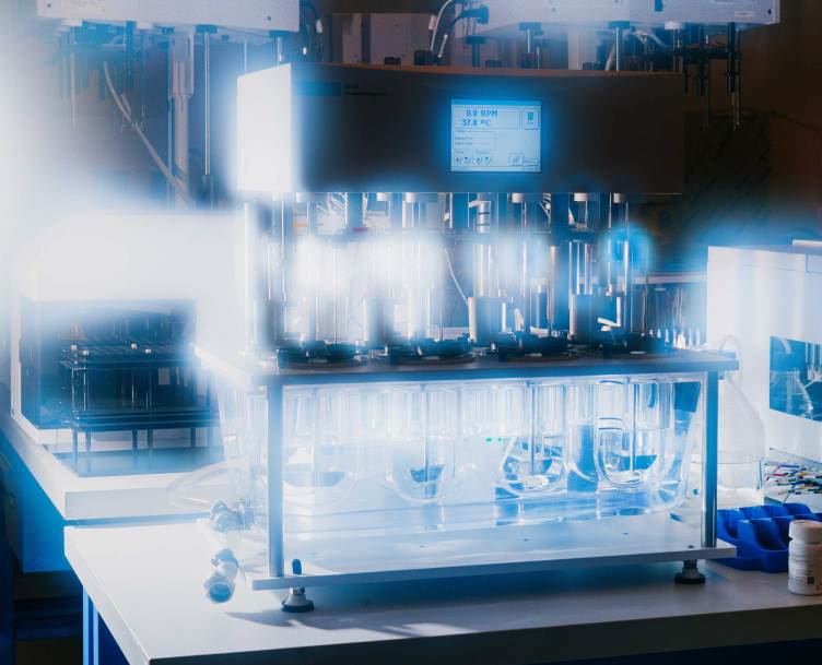 A dissolution machine — several large, clear tubes suspended in a box with metal structures above each of them — dramatically lit.