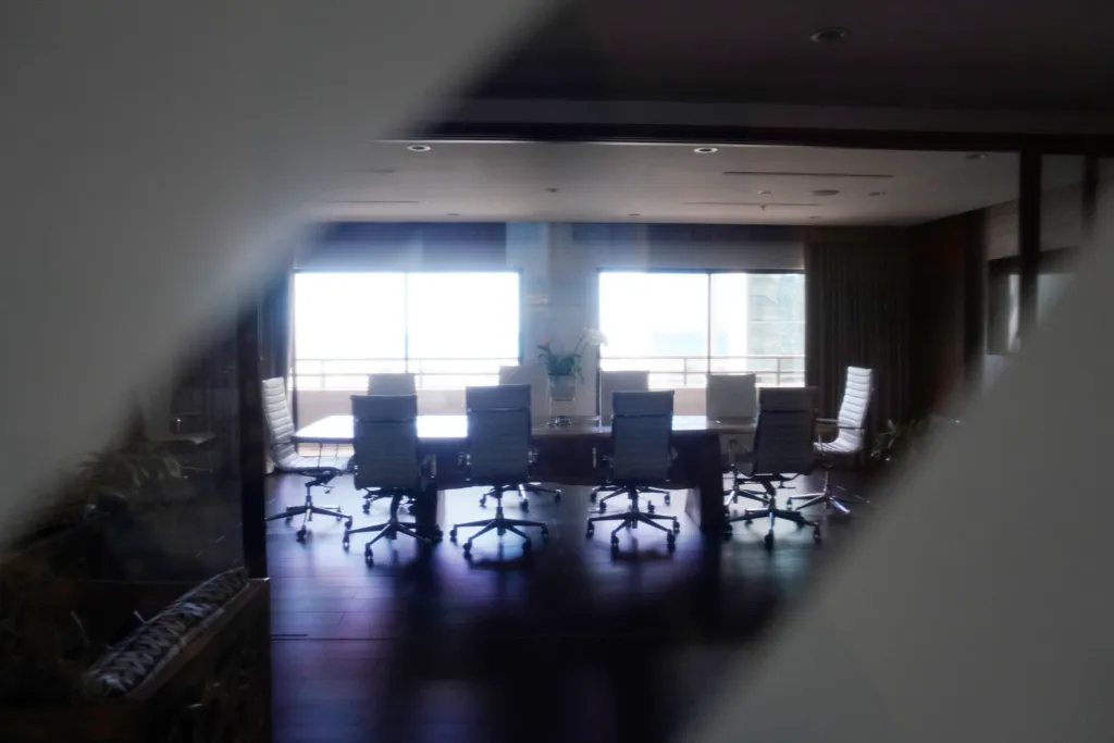 An empty conference room with a large table and numerous office chairs.