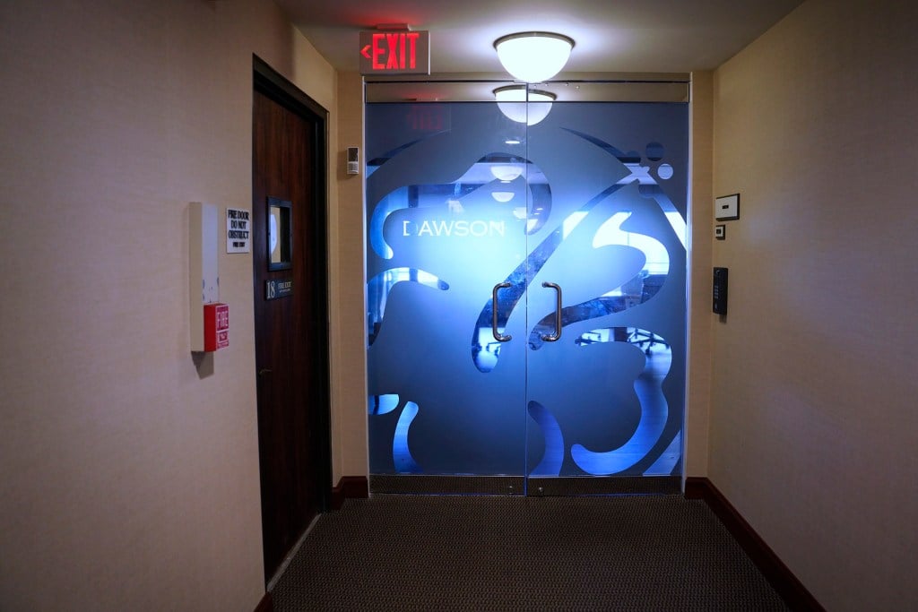 In an office building, a hallway leads to a glass door with an ornate floral design in frosted glass and the word “DAWSON” on it.