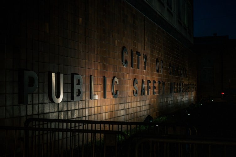 A sign that says “City of Chicago Public Safety Headquarters” on a brown-tiled wall, partially illuminated at night.