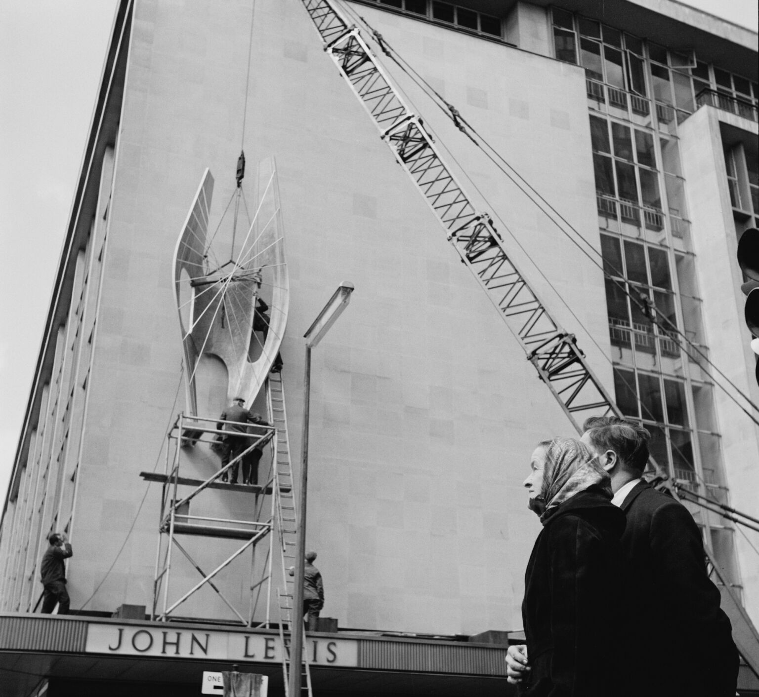 Artist Barbara Hepworth watches her sculpture, Winged Figure, being lowered into position on the side of the John Lewis building 21 April 1963.