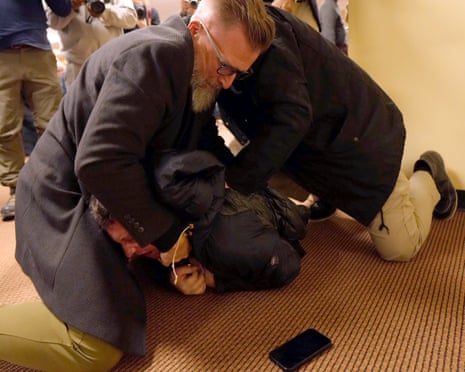 Two men tackle another man on a carpeted floor.