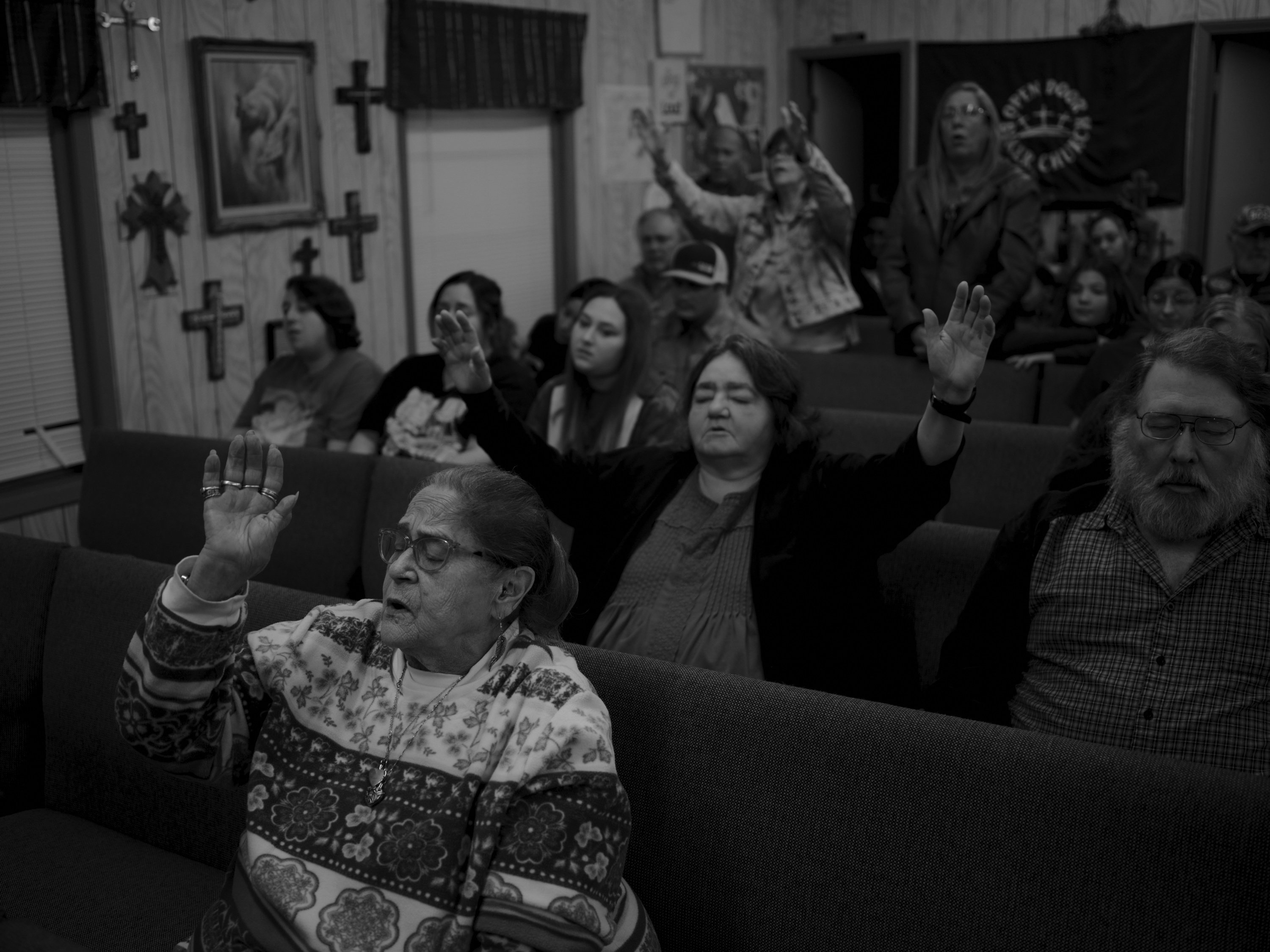 Frauen und Männer schließen ihre Augen und heben ihre Hände zum Gebet, während sie in Holzbänken einer kleinen Gemeindekirche sitzen.
