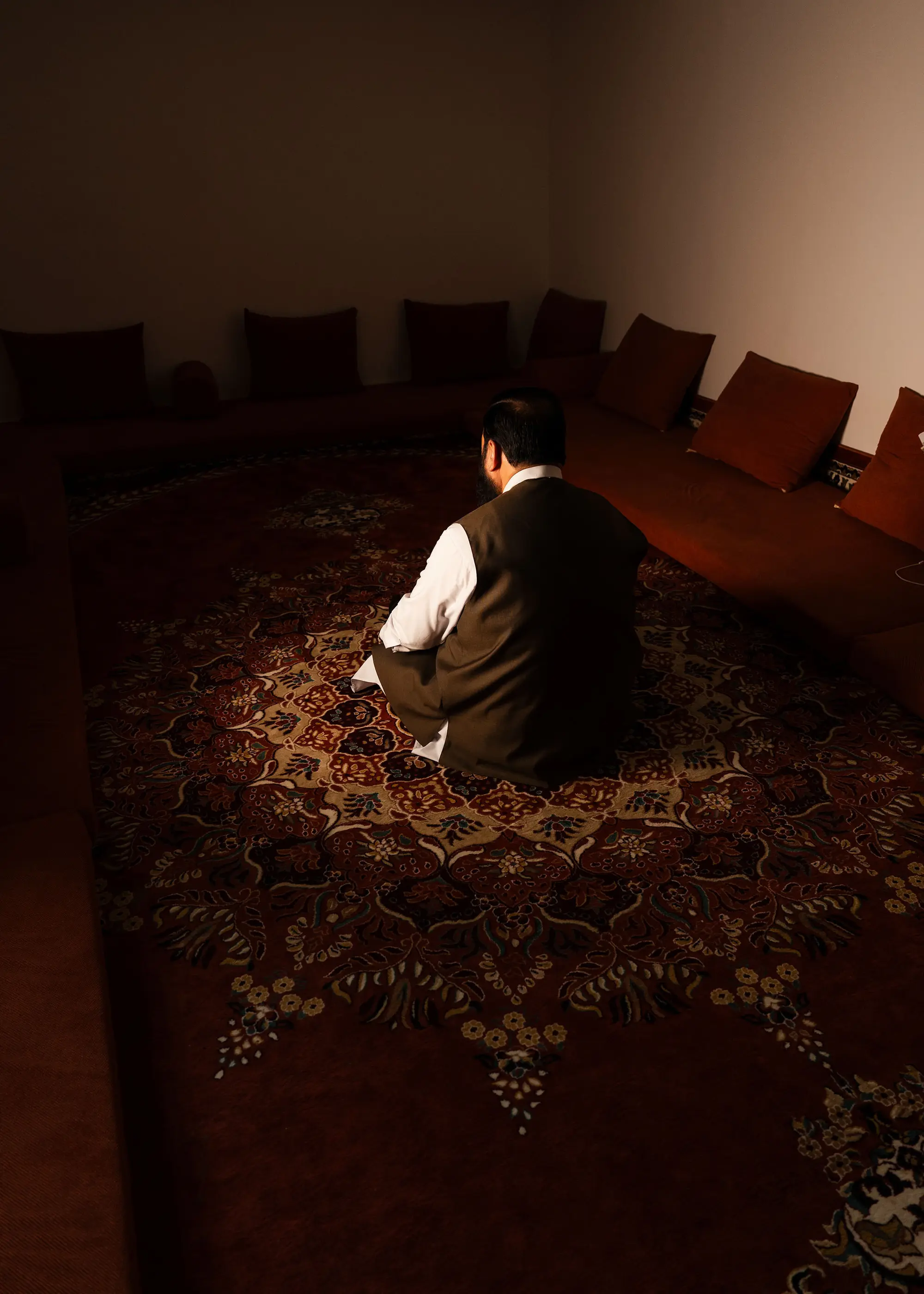 Ein Mann sitzt mit dem Rücken zur Kamera auf einem Zierteppich in einem Gebetsraum.