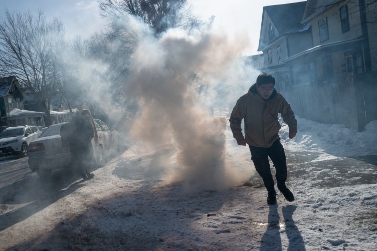 Zwei Menschen zerstreuen sich, als eine Gassäule mitten auf einem verschneiten Bürgersteig in einem Wohngebiet aufsteigt.
