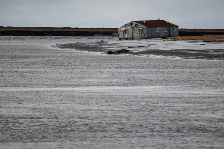 Une maison délabrée d’un étage penche d’un côté, entourée d’eau.