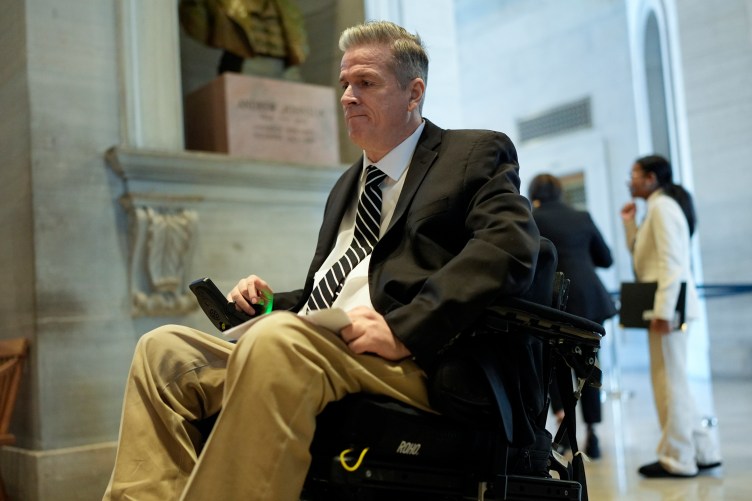 A man in a suit and tie navigates a marble-walled government building using a motorized wheelchair.