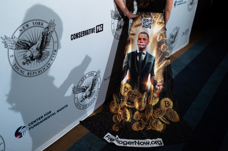 The bottom of a dress has a print that shows Roger Ver with tape over his mouth that says “censored.” The dress print also has a pile of bitcoin, a QR code and the words “FreeRogerNow.org.” The person wearing the dress is posing in front of a backdrop featuring logos from Conservative PAC, New York Young Republican Club and Center for Fundamental Rights.