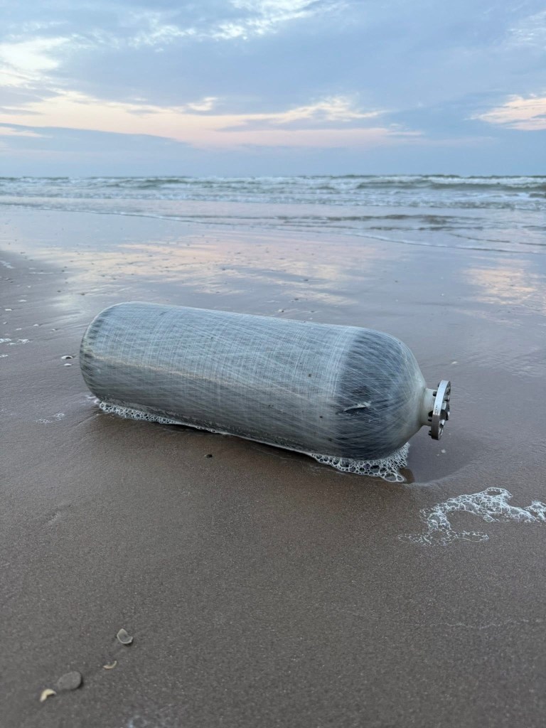 A large metal tank wrapped in a plastic-like material by the water’s edge on a beach.