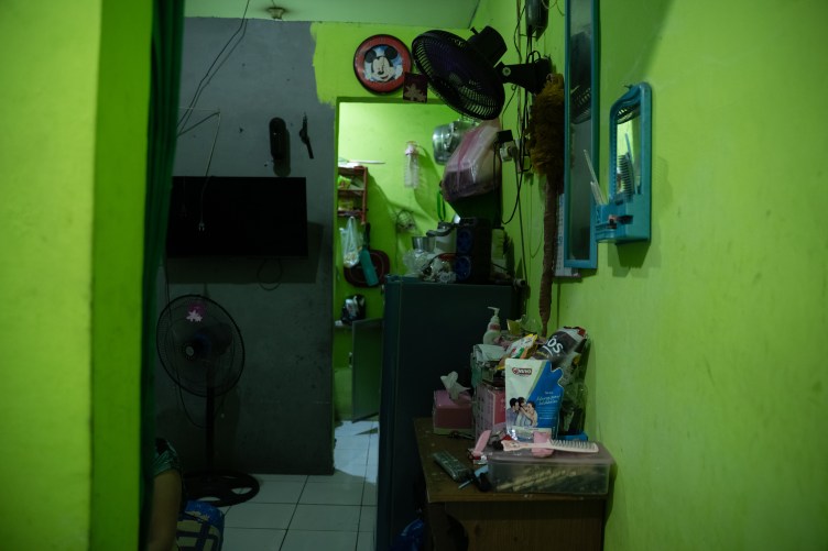 A narrow green room with a tile floor, fans, snacks, two mirrors, a television and a Mickey Mouse clock.