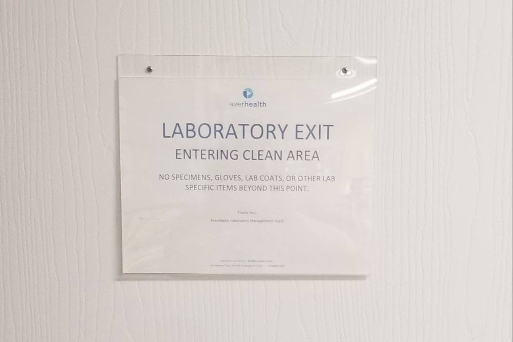 A sign reading “Laboratory exit. Entering clean area. No specimens, gloves, lab coats, or other lab specific items beyond this point.” An Averhealth logo is at the top of the sign.