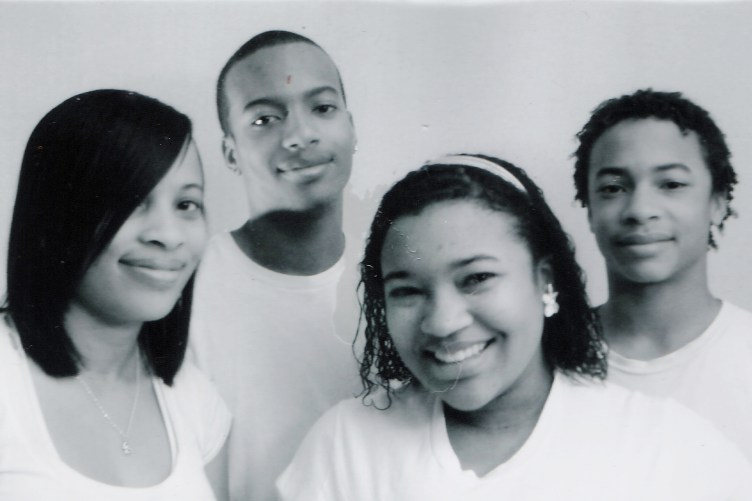 Four young people smiling in a black-and-white family portrait.