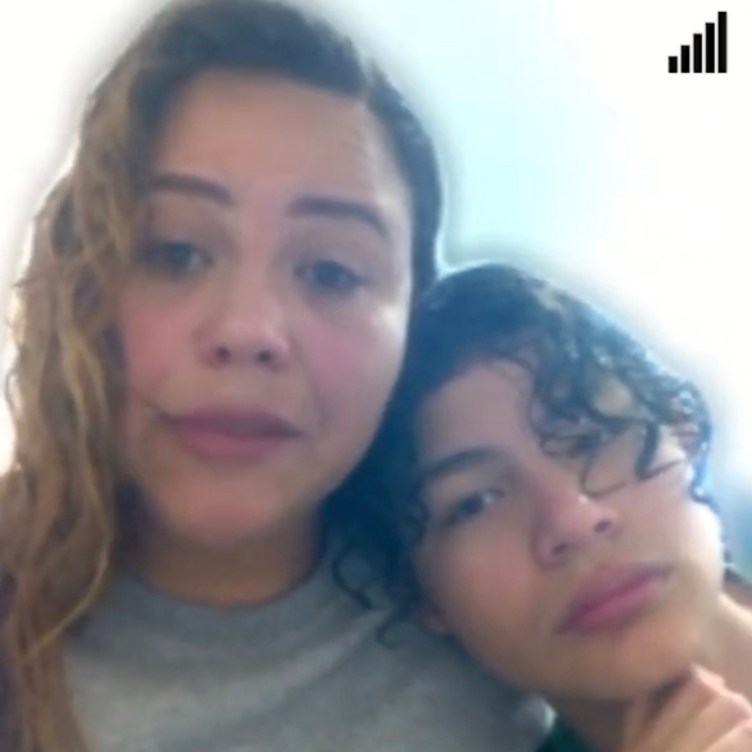 A boy with medium-length wavy brown hair leans his head against the shoulder of a woman with wavy blond hair and bags under her eyes.