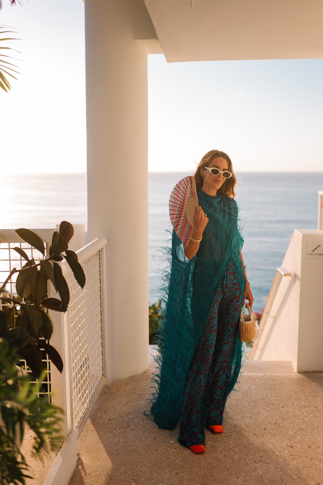 Haut maxi en plumes turquoise, pantalon large imprimé turquoise et sac à main en osier