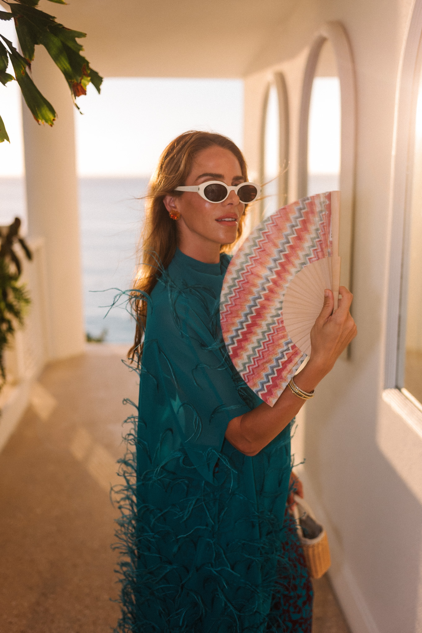 Haut maxi en plumes turquoise, pantalon large imprimé turquoise et sac à main en osier