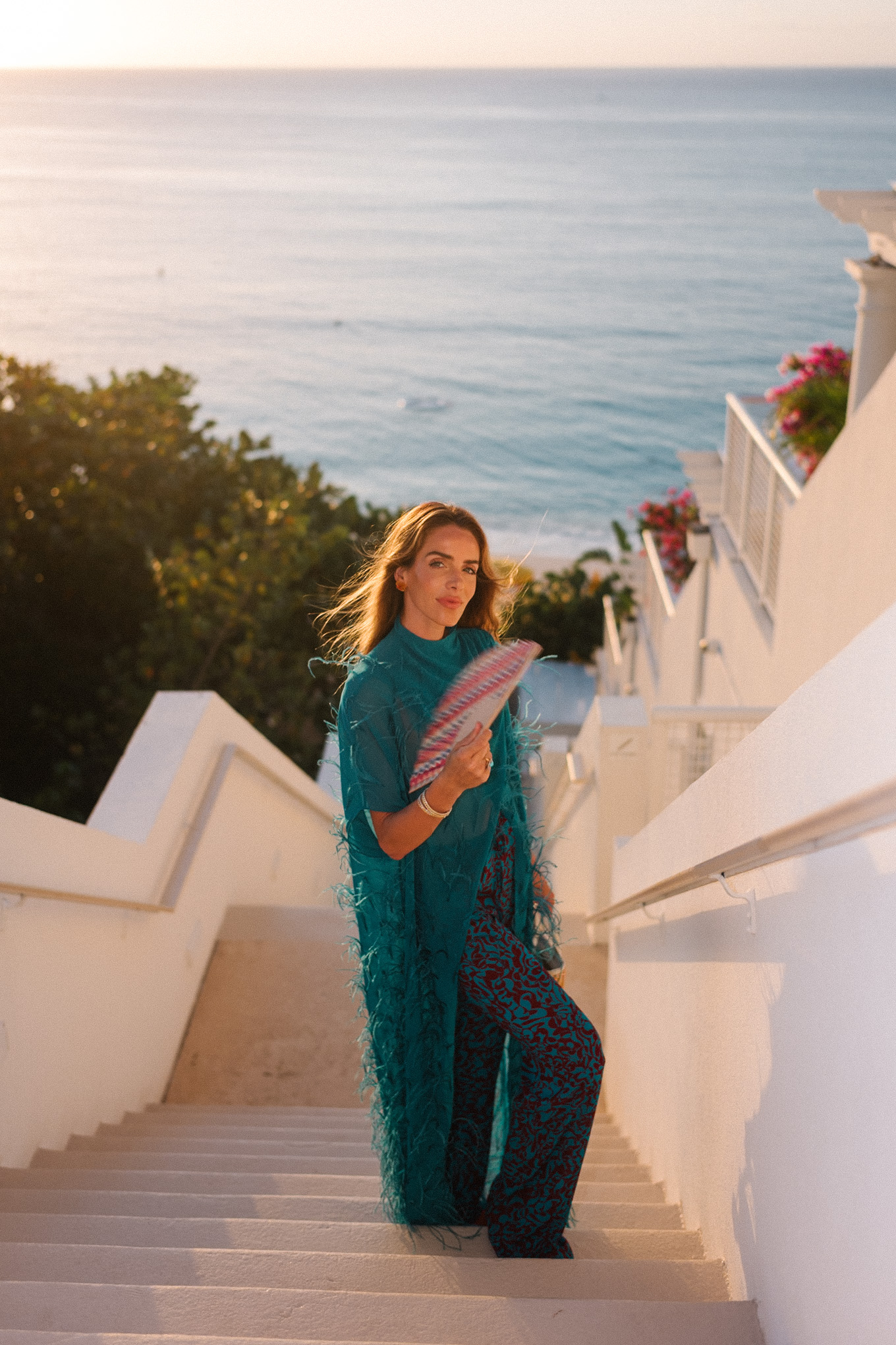 Haut maxi en plumes turquoise, pantalon large imprimé turquoise et sac à main en osier