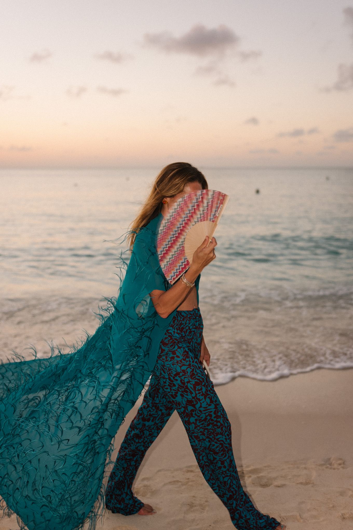 Haut maxi en plumes turquoise, pantalon large imprimé turquoise et sac à main en osier