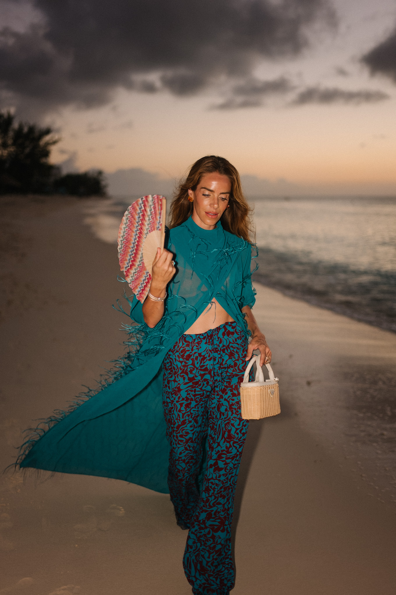 Haut maxi en plumes turquoise, pantalon large imprimé turquoise et sac à main en osier