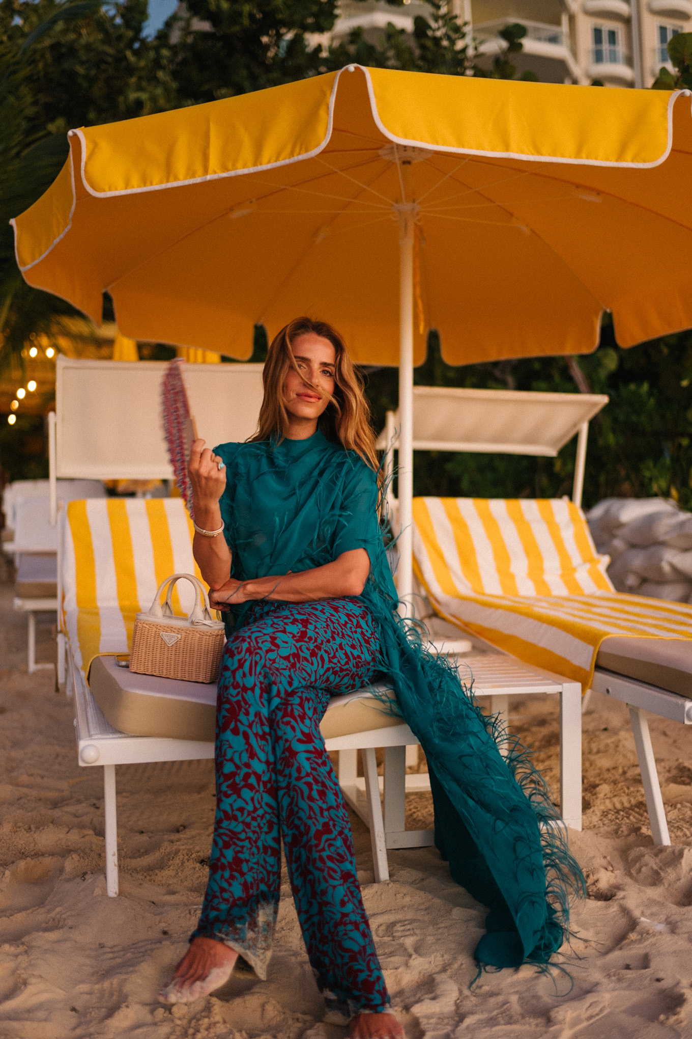 Haut maxi en plumes turquoise, pantalon large imprimé turquoise et sac à main en osier