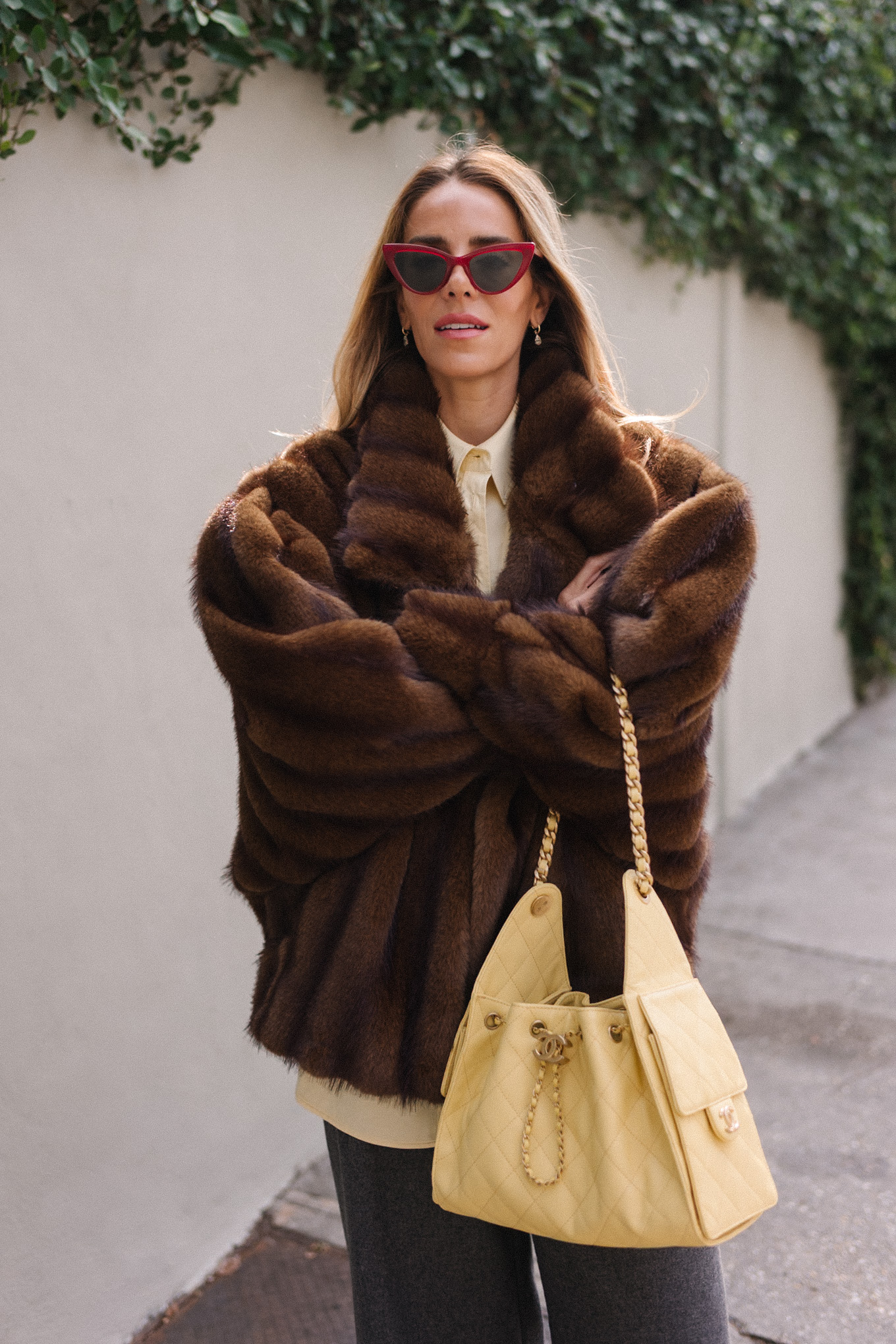 Manteau en fausse fourrure marron, chemise boutonnée jaune, pantalon gris, sac fourre-tout jaune, ballerines rouges