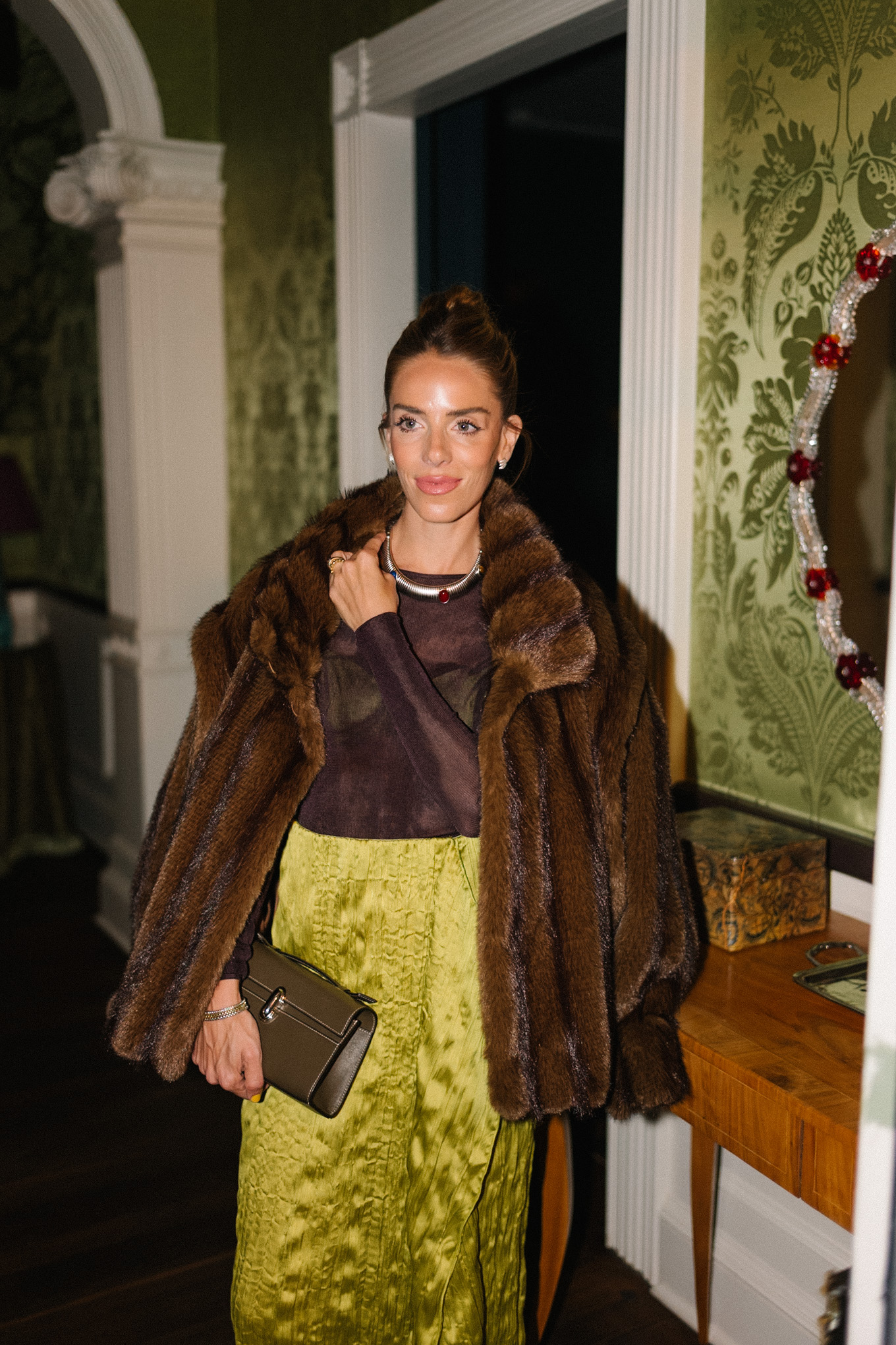 manteau en fausse fourrure marron, haut transparent marron, jupe en soie verte, collants rouges, talons rouges